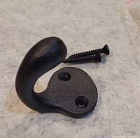 Close-up of one black cast iron wall hook showing curved shape, two screw holes, and one included screw.