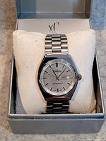 Full front view of the men's silver-tone Selecta wristwatch inside original box with cushioned white pillow.