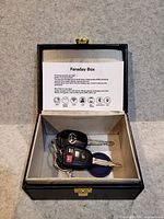 Open shelving box containing two car key fobs and a circular device inside, beige fabric lining visible.