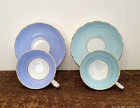 Two sets of vintage teacups and saucers, one set blue textured and one set light blue, each with gold trim.