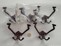 Six vintage cast iron hooks, some in clear plastic bags, arranged with a coin to indicate size.