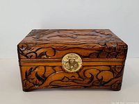 Closed view of vintage Asian wooden box showing carved detailed motifs on lid and sides, with visible brass lock.