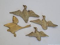 Four vintage brass duck wall plaques arranged on a flat surface showing their detailed feather texture and shapes