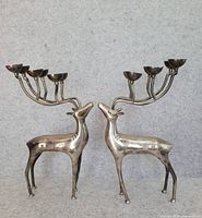 Pair of silver plated brass stag candlesticks with three-cup candle holders on branched antlers, standing side-by-side against gray background.