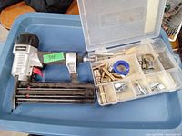 Air nailer tool alongside a container with multiple brass and metal air fittings and a roll of blue sealing tape.