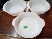 Three white opalware bakeware dishes arranged together showing floral pattern and handles
