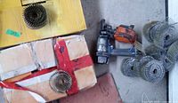 Photo showing one pneumatic Brad Nailer and multiple coils of nails arranged on the ground near cardboard boxes.