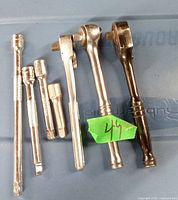 Photo of seven metallic drive ratchets and socket extensions with a green label marked '44'