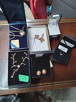 Overview of assorted costume jewelry pieces on wooden table including necklaces, earrings, and rings in their boxes