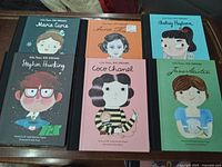 Photo of six Little People Big Dreams hardcover books arranged on a surface, featuring Marie Curie, Anne Frank, Audrey Hepburn, Stephen Hawking, Coco Chanel, and Jane Austen.