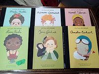 Photo showing all six Little People Big Dreams books with illustrated covers of Frida Kahlo, Vivienne Westwood, Harriet Tubman, Rosa Parks, Jane Goodall, and Amelia Earhart.