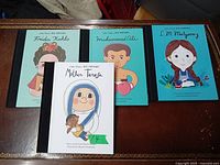 Four Little People Big Dreams books arranged on a table showing covers featuring Frida Kahlo, Muhammad Ali, L.M. Montgomery, and Mother Teresa.