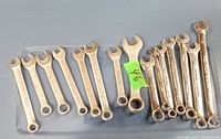 16 metric combination wrenches arranged in two parallel rows on a flat surface. Wrenches show signs of usage.