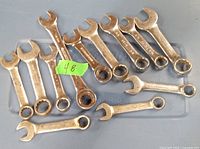Photo showing 11 small combination wrenches including metric and SAE sizes, metal finish with markings, arranged on a flat surface.