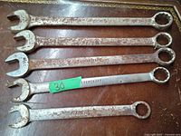 Top view of five used SAE combination wrenches arranged in a row showing surface rust and wear