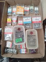 Top view of mixed hardware packs in cardboard box showing assorted nails, screws and fasteners largely in HandyPack brand plastic packs and containers, various sizes and types.