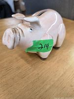 Side view of the ceramic piggy bank showing the pink pig shape, painted details, and green sticker '214'