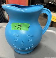 Front view of blue Kool-Aid pitcher jug showing the embossed Kool-Aid Man face and handle.