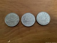 Three Canadian one dollar coins dated 1968, 1972, and 1983 showing the reverse side with the Voyageur design.
