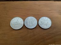 Reverse sides of the three coins showing different Canadian themed designs: 1971 Bluenose schooner, 1975 shield with maple leaves and wheat, 1986 voyageur canoe