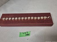 Gold tone rhinestone bracelet laid flat on a rectangular maroon box, showing full length and clasp.