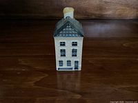Front view of the KLM Delft Blue Dutch house #26 porcelain bottle showing detailed windows and door, tiled roof, and chimney.