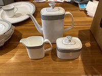 Coffee pot, creamer, and sugar bowl set displayed on wood surface, showing overall appearance.