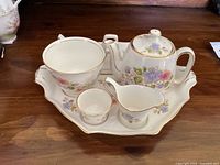 Full view of the breakfast set on the octagonal tray showing teapot, cup, creamer, egg cup, and toast rack with floral decoration and gold trim.