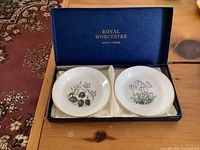 Two round Royal Worcester bone china coasters in a blue box with white interior lining, showing floral designs on each coaster.