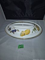 Top view of the covered serving dish showing fruit decoration on lid including lemons and plums, gold trim around edges.