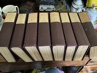 Eight hardcover volumes lined up horizontally showing dark brown cloth bindings with cream title labels on spine.