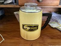 Full view of the yellow Spunshine aluminum coffee percolator with black handle and glass lid on a wooden surface.