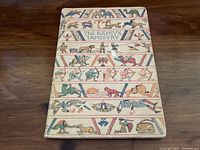 Front cover of The Bayeux Tapestry book showing colorful medieval-style illustrations featuring animals and human figures in panels.