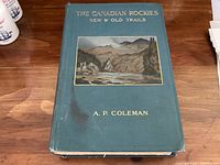 Image of the front cover of 'The Canadian Rockies New & Old Trails' book by A.P. Coleman, showing the title, author, published year, and colored mountain illustration.