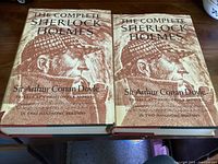 Photo showing front covers of both volumes with illustrated dust jackets featuring Sherlock Holmes sketch.