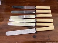Six butter spreaders laid out horizontally on wooden surface showing entire set and handles