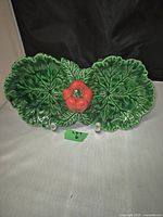 Front view of the green ceramic dish shaped as two leaves with a red pepper in the center.