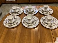Full view of all 6 place settings, each with 5 pieces including plate stack and cup on saucer, showing the floral pattern and gold trim on Wedgwood Charlotte china.