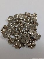 Cluster of small 10KT gold earring backs with floral-shaped edges and central holes, laying on a white surface.