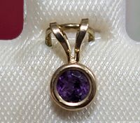Close-up front view of the 14K gold pendant with a round amethyst gemstone in bezel setting on a white textured background.