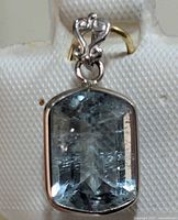 Close-up photo of 14KT gold pendant featuring a rectangular faceted aquamarine gemstone with decorative bail.