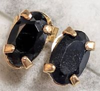 Close-up photo of two oval faceted black diamonds with 14KT gold prongs in stud earring style.