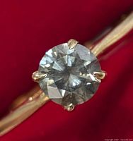 Close-up view of round natural diamond in gold prong setting on red background.