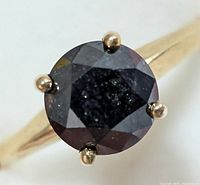 Close-up view of round black diamond held by four prongs on gold band, showing faceted diamond surface