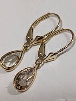 Close-up image of the pair of gold earrings with teardrop-shaped diamonds. Shows detailing of the lever-back clasp and bezel setting for the stones.