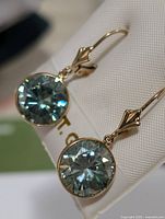 Close-up front view of earrings showing bezel-set round moissanite stones and decorative bail