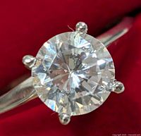 Front close-up of round brilliant moissanite held in four-prong setting against red background