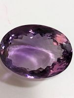 Close-up image of a large, faceted oval amethyst gemstone with deep purple hues showing reflective facets.