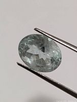 Close-up photo of a faceted oval aquamarine gemstone held by tweezers highlighting facets and inclusions