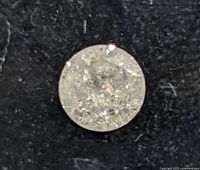 Close-up front view of the loose round-cut diamond showing clear facets on a black background.